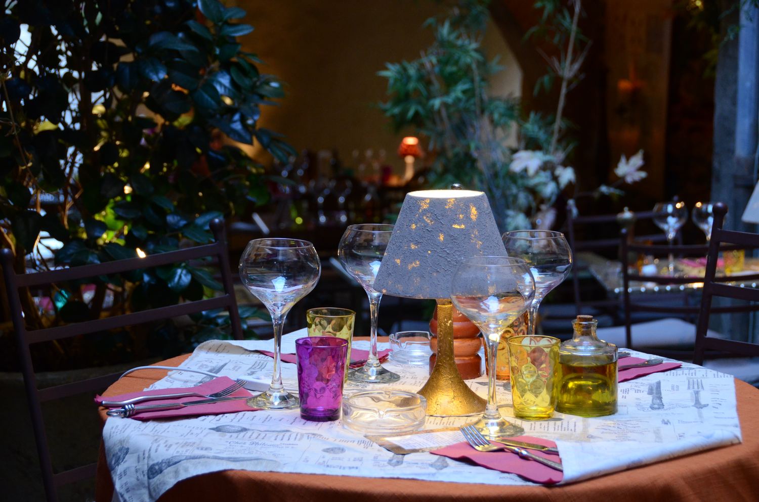 Une table dressée le soir sous la voûte, avec une lampe allumée et des verres colorés